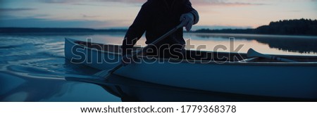 CU view of a paddle, man canoeing alone boat on a large lake at dawn Royalty-Free Stock Photo #1779368378