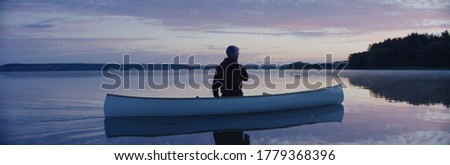 Man canoeing in a traditional wooden boat on a large lake at dawn Royalty-Free Stock Photo #1779368396