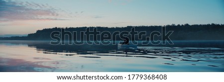 Man canoeing in a traditional wooden boat on a large lake at dawn Royalty-Free Stock Photo #1779368408