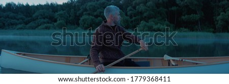 Portrait of mid 50s man canoeing alone boat on a large lake at dawn Royalty-Free Stock Photo #1779368411
