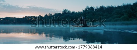 Man canoeing in a traditional wooden boat on a large lake at dawn Royalty-Free Stock Photo #1779368414
