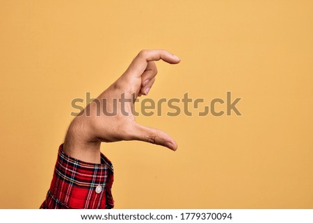 Hand of caucasian young man showing fingers over isolated yellow background picking and taking invisible thing, holding object with fingers showing space