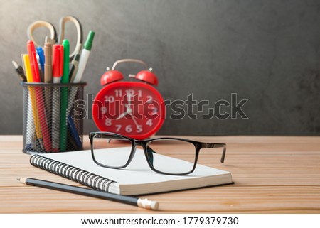 Notebooks, pens, pencil holder, glasses, Red alarm clock on wooden desks and loft walls with sunlight and copy space
