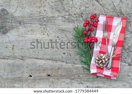 Merrry Christmas background. Vintage fork and knife, holly berries and fir twig on checkered napkin and rustic wooden background. Space for text, flat lay