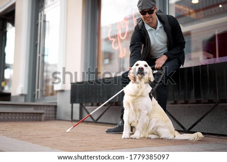 25 years old man suffer from blindness, get help by dog guide, sit having rest outdoors