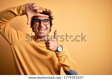 Young handsome man wearing casual t-shirt and glasses over isolated yellow background smiling making frame with hands and fingers with happy face. Creativity and photography concept.