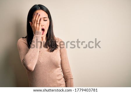 Young brunette woman with blue eyes wearing casual sweater over isolated white background Yawning tired covering half face, eye and mouth with hand. Face hurts in pain.