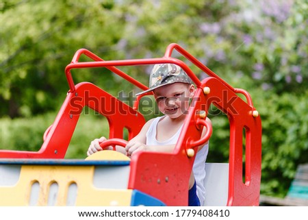 Smiling boy in white T-shirt and cap plays in the playground in the summer outdoors