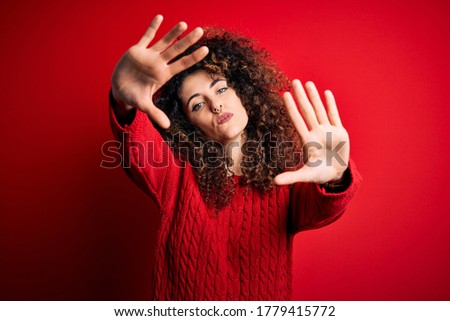 Young beautiful woman with curly hair and piercing wearing casual red sweater doing frame using hands palms and fingers, camera perspective