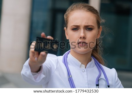 Portrait of a sad tired girl doctor holding a plastic card in front of the camera. Close-up of a nurse holding a map in front of the camera
