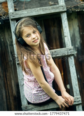 Cute little girl enjoys music with headphones in the village outdoors.