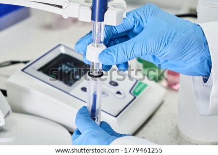 Woman in a rubber gloves holding a glass electrode for measuring of pH of the solution using pH meter. Analytical or electro chemistry laboratory.  Royalty-Free Stock Photo #1779461255