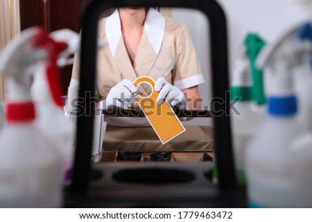 Room service.A uniformed maid holds an unmarked sign for guests. Copy space. Unrecognizable photo.Truck for the maid.