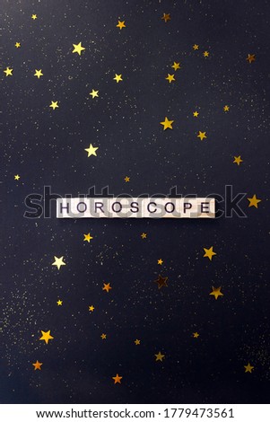 Word Horoscope. Wooden blocks with letters on dark blue background decorated with gold star confetti. Vertical poster, selective focus.