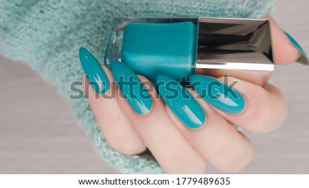 Woman's hands with long nails and turquoise blue manicure with bottles of nail polish