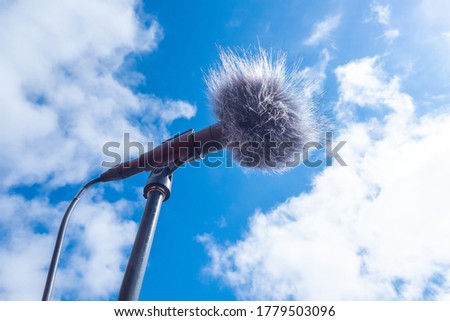 Microphone in windproof. Microphone on sky background. Stand mike is on the street. Gray fur on a microphone for protection from wind. Concept - sale windproof for mike. Sound equipment.