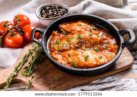 Baked halibut fish in a pan with tomato sauce. White wooden background. Top view