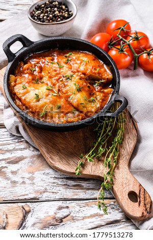 Tilapia fish baked in tomatoes in a pan. White wooden background. Top view