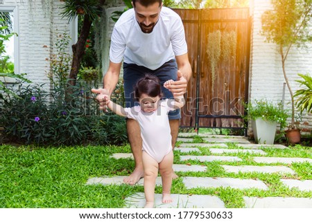 Adorable little baby daughter practice and learning walking that first time toddler girl walk on grass by father holding hands and teaching her walking at front yard. Infant baby get determined Royalty-Free Stock Photo #1779530633