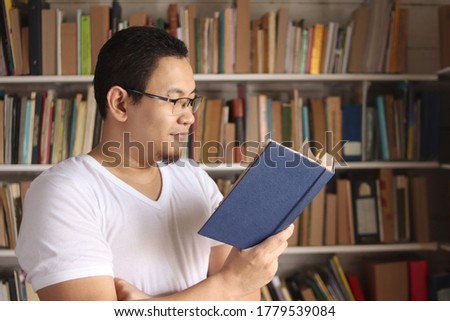Asian man reading book in library, educational concept. Happy smiling expression when doing leisure activity