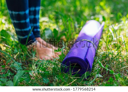 Woman standng next to yoga mat in a summer park wearing sports wear going to do some yoga exercises. Close up