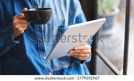 Closeup image of a woman holding and using tablet pc with drinking coffee 