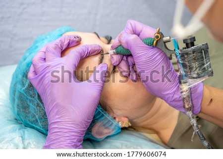 Beautiful woman making permanent makeup in cosmetology salon.