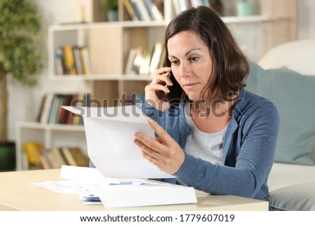 Serious adult woman checking letter calling on smart phone sitting in the livingroom at home