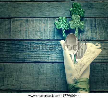 St. Patrick's Day Green Shamrocks and Silverware with white Napkin on Rustic Wood Background with room or space for copy, text, words.  Vintage camera instagram treatment.