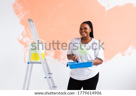 Beautiful african american girl painting the wall with paint roller. Portrait of a young beautiful woman painting wall in her new apartment. Redecoration and renovation concept. Royalty-Free Stock Photo #1779614906