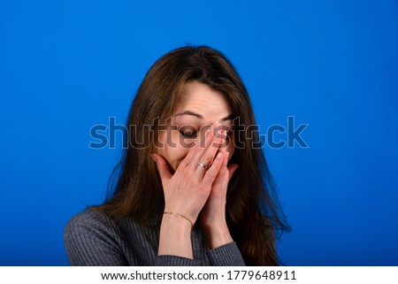 Photo of smiling, cheerful young female in grey dress on blue background. Emotional portrait