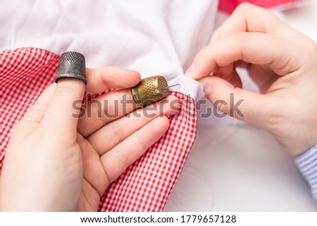 The girl holds a needle and two thimbles in her hands. Vintage thimble. Sewing. Against the background of pink and white fabric. Royalty-Free Stock Photo #1779657128