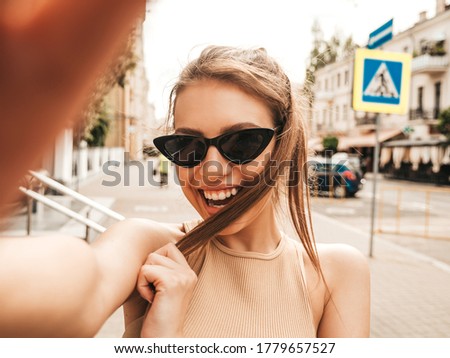 Portrait of beautiful smiling brunette woman in summer clothes. Model taking selfie on smartphone.Woman making photos in warm sunny day in the street in sunglasses. Cheerful female going crazy