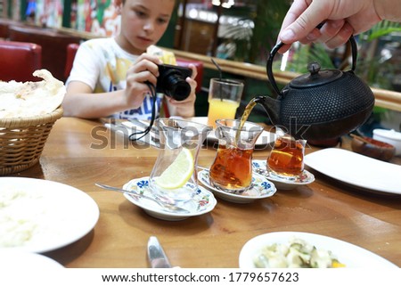 Child takes pictures of how person pours tea in restaurant