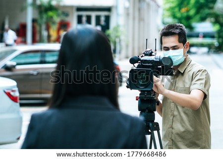 Young cameraman using a professional camcorder outdoor filming news while wearing mask prevent Covid-19 or coronavirus quarantine pandemic. Royalty-Free Stock Photo #1779668486