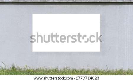 white frame mock-up hanging on concrete wall over pavement with grass front view