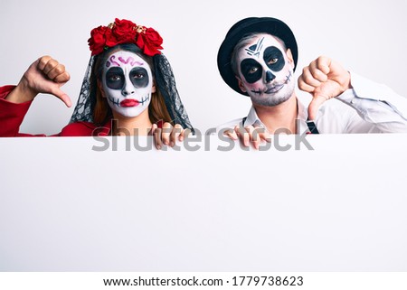 Couple wearing day of the dead costume holding blank empty banner with angry face, negative sign showing dislike with thumbs down, rejection concept 