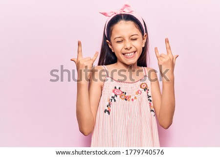 Beautiful child girl wearing casual clothes shouting with crazy expression doing rock symbol with hands up. music star. heavy concept. 