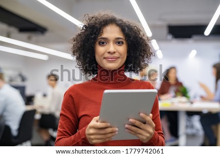 Portrait of happy multiethnic businesswoman using digital tablet in agency. Successful business woman in casual clothing working on tablet. Mixed race young woman looking at camera in creative office. Royalty-Free Stock Photo #1779742061