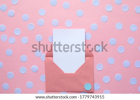 white blank card in envelope on pink background with blue confetti. Holiday mockup. Top view.