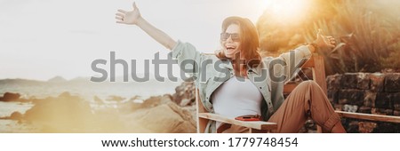 Outdoor summer smiling lifestyle portrait of pretty young woman having fun in with camera travel photo of photographer Making pictures in hipster style glasses and hat, stylish outfit