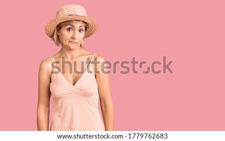 Young blonde woman wearing summer hat looking sleepy and tired, exhausted for fatigue and hangover, lazy eyes in the morning. 