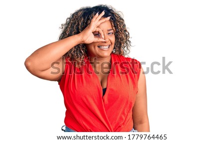 Young african american plus size woman wearing casual style with sleeveless shirt doing ok gesture with hand smiling, eye looking through fingers with happy face. 