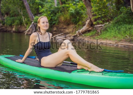 Side view picture of a woman sitting and relaxing on the sup board. Surfer woman resting