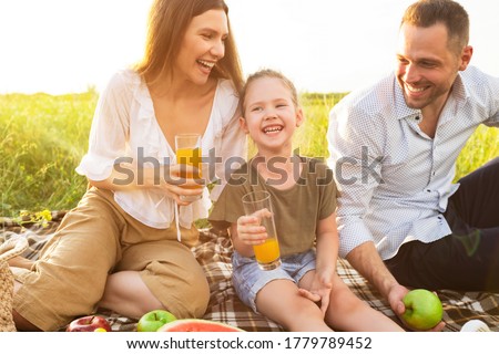 Healthy Beverages. Portrait of laughing family sitting on blanket and drinking orange juice from glasses