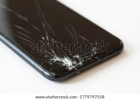 Corner of mobile cell phone with broken display screen after drop. Crashed black smartphone close-up. Perspective image on white background.