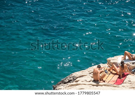 Group of friends lying on some rocks of the Calanques de Marseille sunbathing on vacation in front of the turquoise blue Mediterranean sea during a sunny summer day in the blue coast France