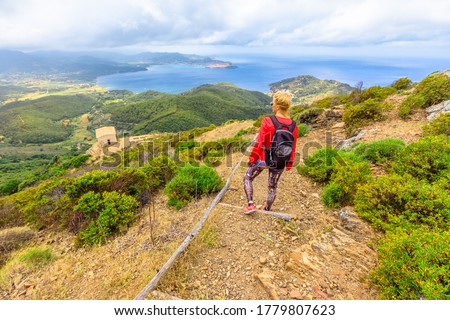 Hiking to Volterraio Castle. Backpacker woman looking views of Portoferraio Gulf, Elba Island. Stone stairs along Monte Volterraio with medieval fortress dominates.Tourism in Tuscany Italy destination Royalty-Free Stock Photo #1779807623