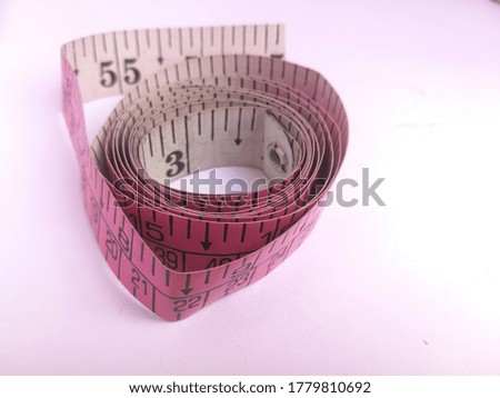 A winded tailoring tape placed isolated in a white background.The tape has marking on it.The tape has pink color outside and white color inside.