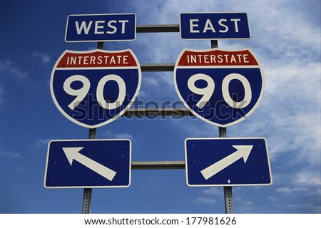 This is a road sign on the New York State Freeway. It points out the direction for Route 90 to go east or west. The signs are blue, red and white against a blue sky. Royalty-Free Stock Photo #177981626